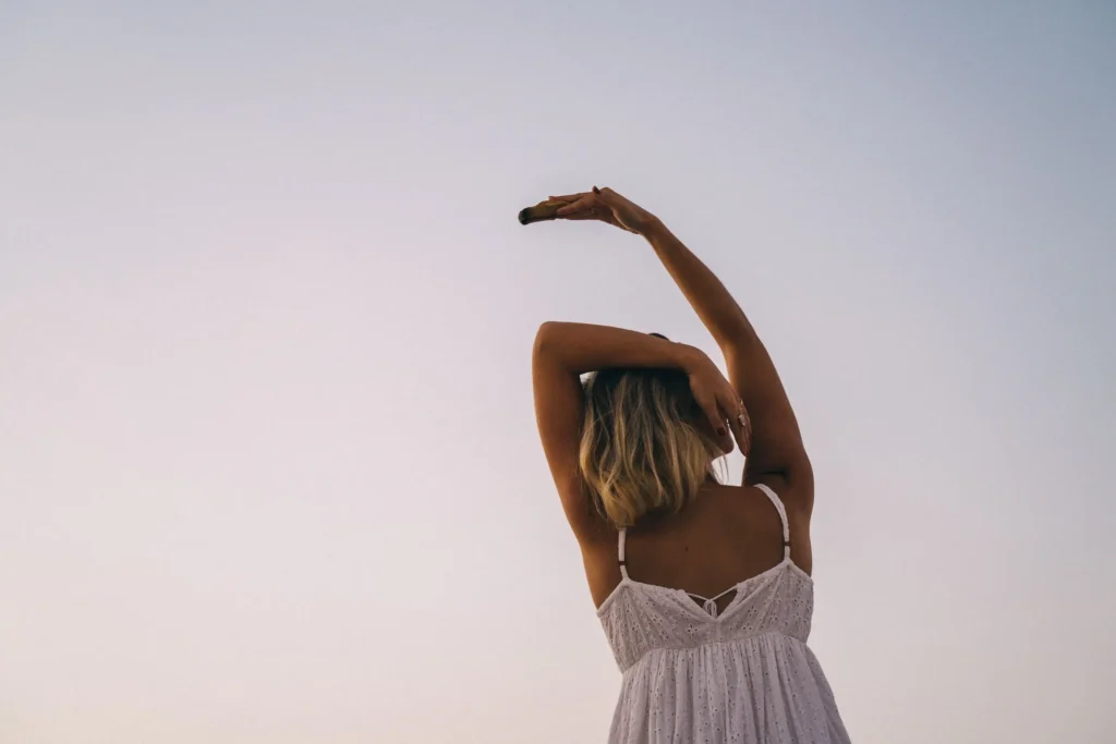 Femme les bras levés vers le ciel au coucher du soleil, geste d'ouverture pour attirer la chance